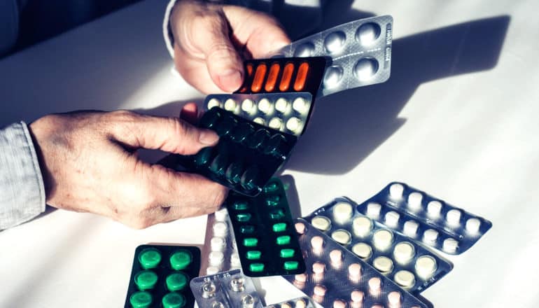 older person's hands hold assorted blister packs of pills