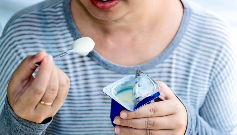 A woman in a striped shirt eats yogurt from a blue container