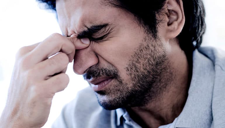 A man pinches the bridge of his nose in pain