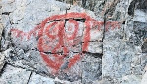 A red painting of what looks like an animal's face with antlers on a cave wall