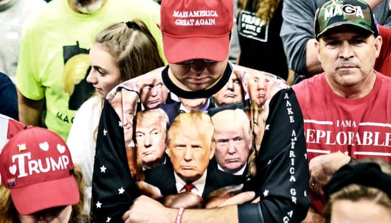 A man wears a red Trump hat and a shirt with many images of the president's face