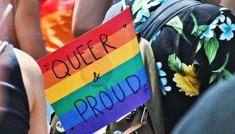 "queer and proud" written on pride flag