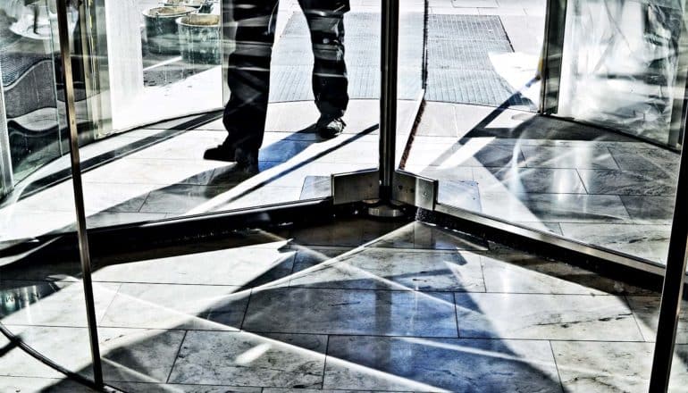 A man walks into a building through a revolving door, with only his lower legs and feet visible