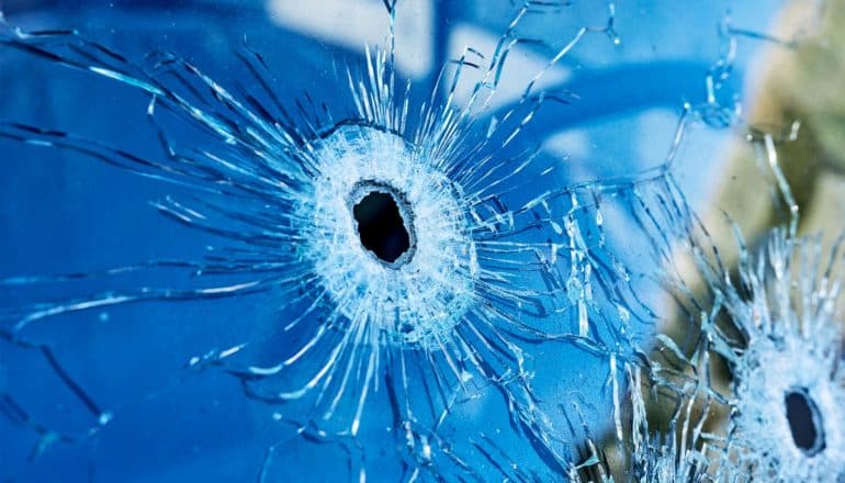 2 bullet holes in glass reflecting blue light