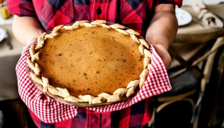 A person in a red flannel shirt holds an orange pumpkin pie with a tea towel