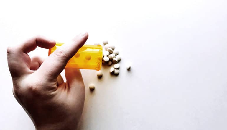 A hand pours a bottle of pills onto a white surface