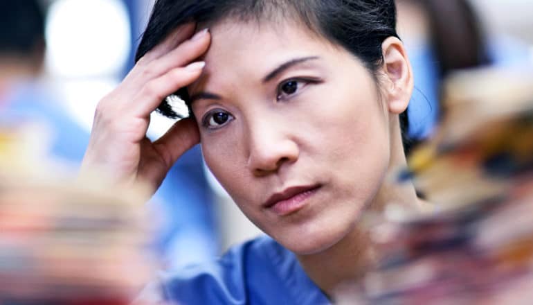 A hospital worker puts her hand to her forehead while looking at a stack of medical files