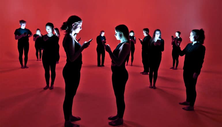 A group of people in black clothes look down at their phones against a red background