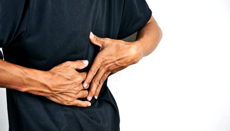 A person grabs at their stomach in pain in a black t-shirt against a white background