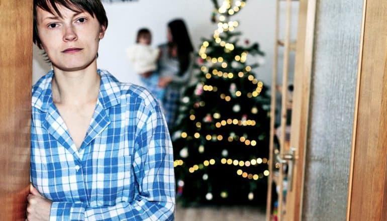 person leans in doorway, blurry person holds child by xmas tree in background