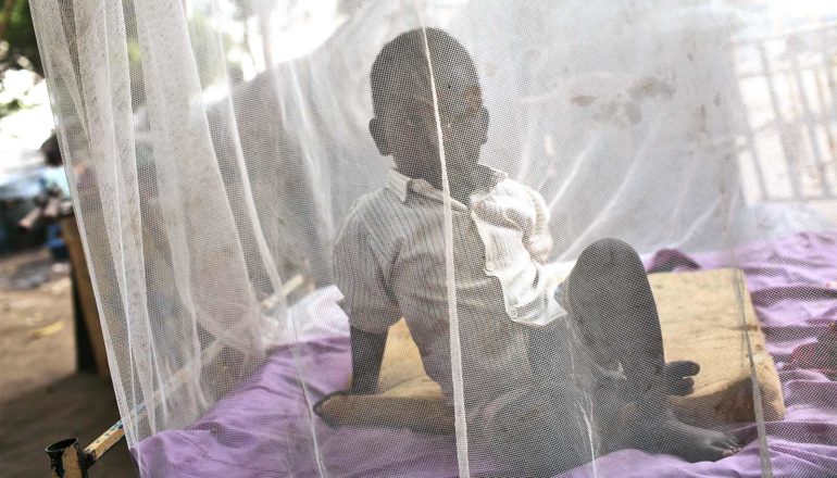 A young boy sits under a white malaria bed net