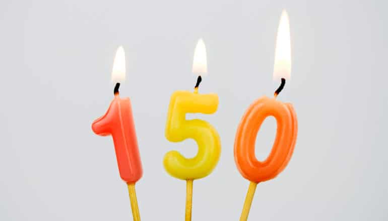 orange and yellow birthday candles of the numbers 1, 5, and 0 are lighted and burning against a gray background