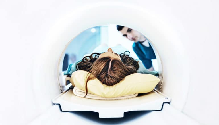 A woman lays on a MRI scan table, viewed from within the MRI machine so only the top of her hair is visible