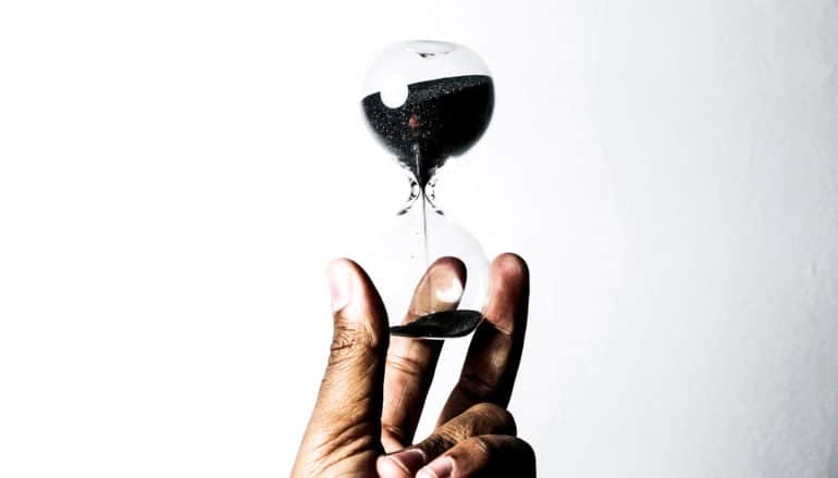 A person holds an hourglass with dark sand inside against a white background