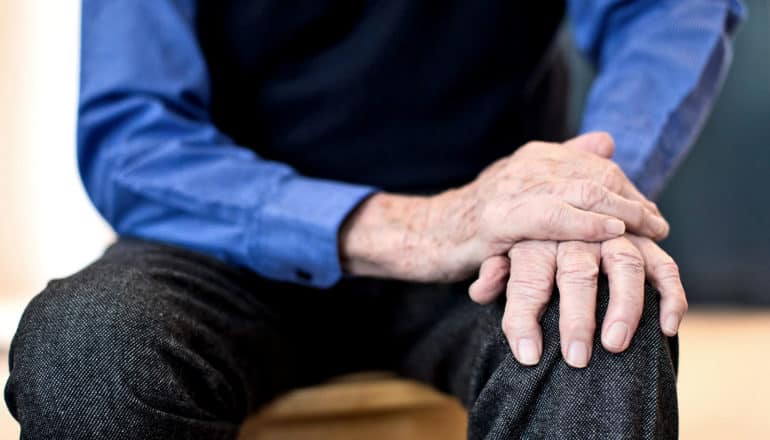 older person holds hand down on knee, as if to quell tremor