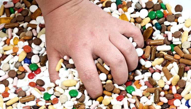 A kid's hand reaches into a pile of pills to grab a handful