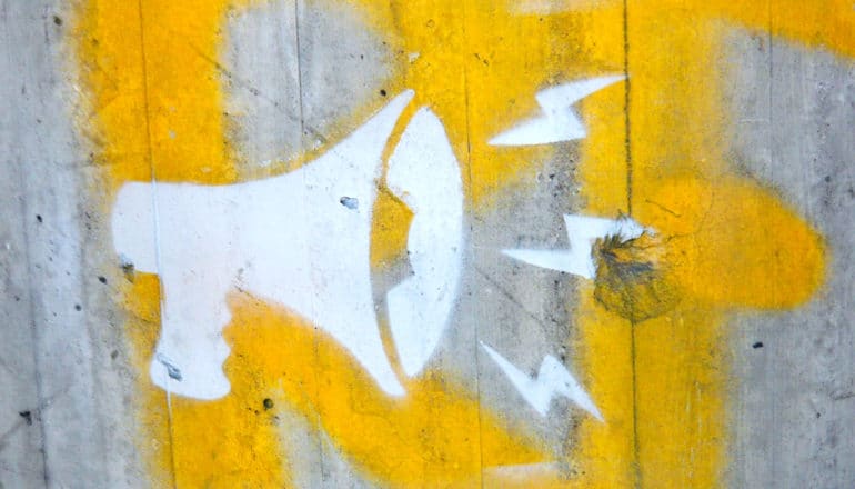 A megaphone is painted on a concrete wall in white, with some yellow paint on the wall behind it