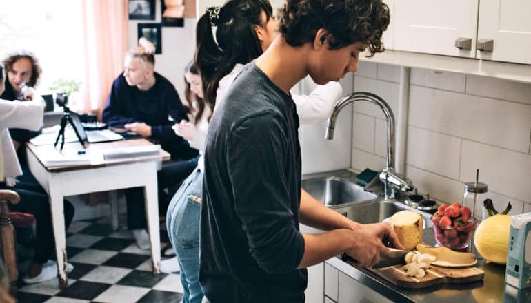 teen cuts fruit in kitchen among other people