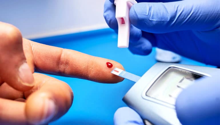 A person has a drop of blood coming from their fingertip as a gloved doctor uses a blood sugar test on them