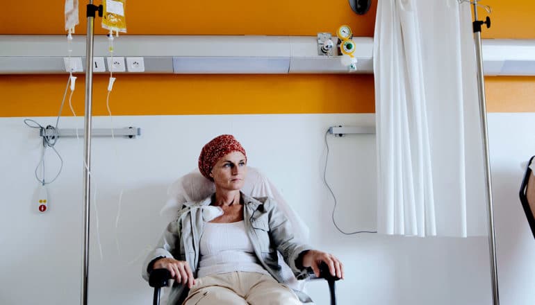 A woman gets chemotherapy treatment in a hospital while looking into the distance, the wall behind her half white and half yellow