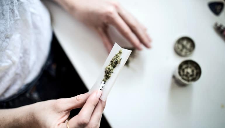 A woman puts marijuana into a rolling paper to roll a joint