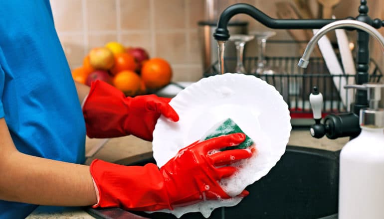 person in red rubber gloves washes plate in sink