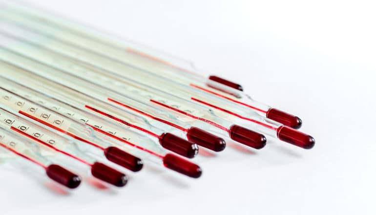 A set of 10 glass thermometers sit together at a diagonal angle on a white background