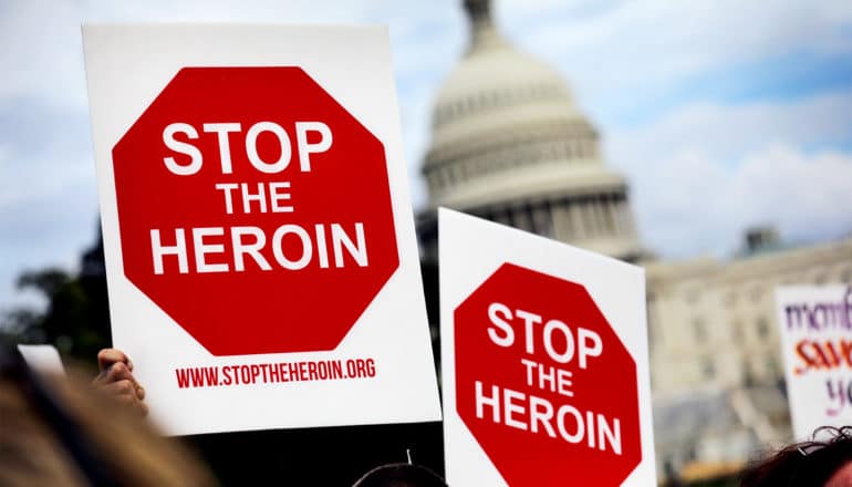 Two people hold up signs that read "Stop the Heroin" with the US Capitol building in the background