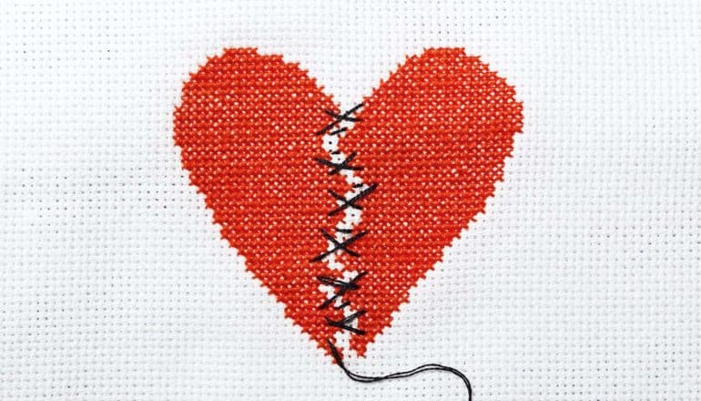 A crossstich of a broken heart mended with black thread