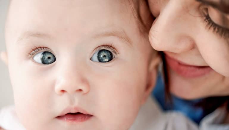 adult speaks into wide-eyed baby's ear