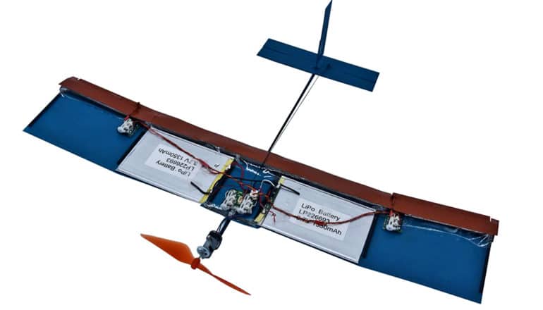 A small fixed-wing drone sits on a white background. The drone has an orange propeller on its nose, two flat wings with battery packs on them, and an airplane-like tail