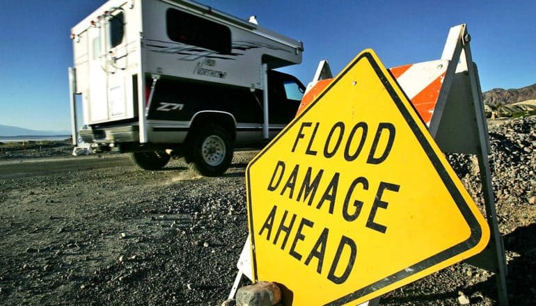 RV drives past "flood damage ahead" sign on road