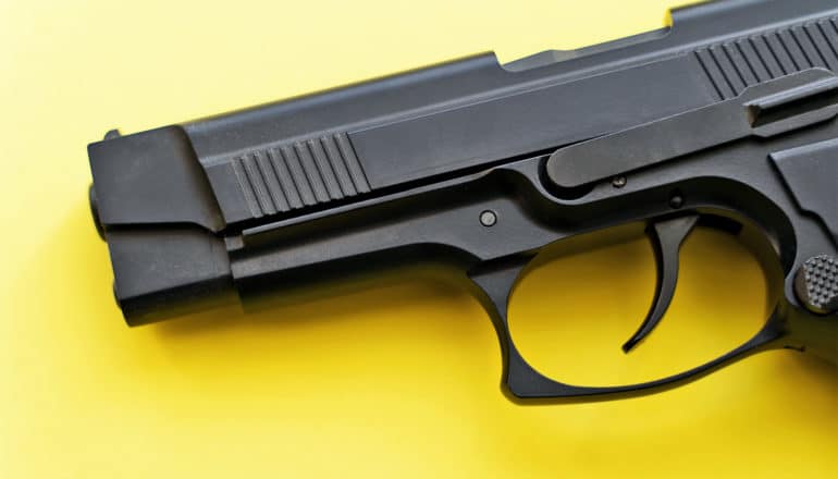 A black handgun sits on a yellow background