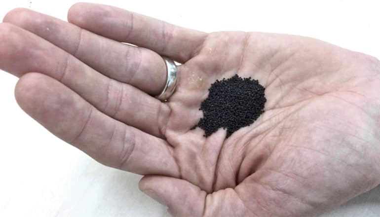 A person holds the mineral-coated sand in their palm. It looks black against their skin