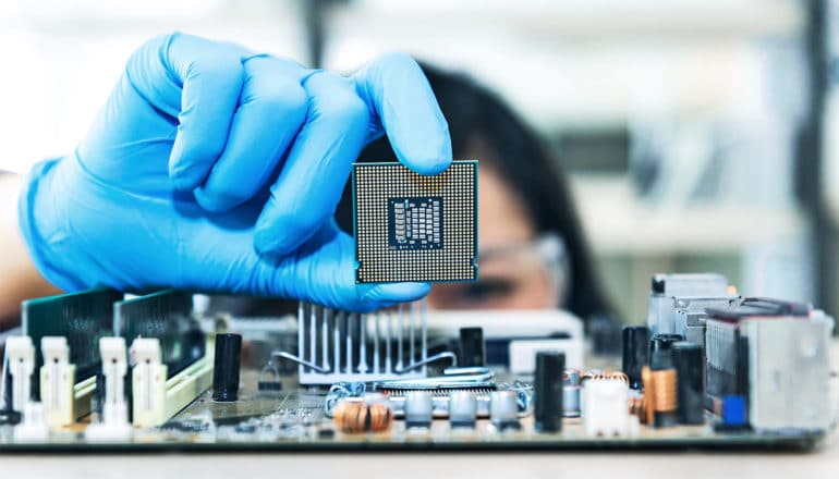 A researcher wearing blue gloves holds up a microchip between her thumb and index finger