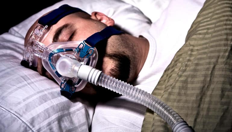 A sleeping man wears a CPAP mask for sleep apnea