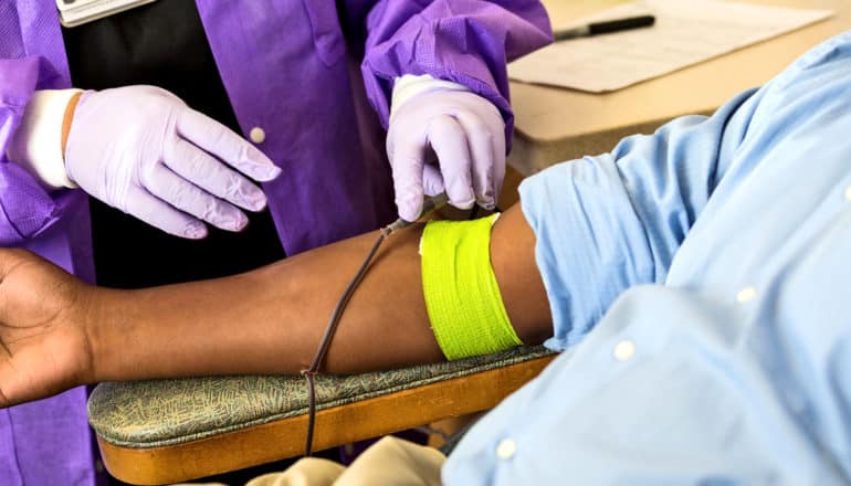 person in lab coat and gloves draws blood