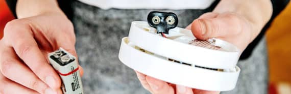 A woman holds a carbon monoxide detector and its battery