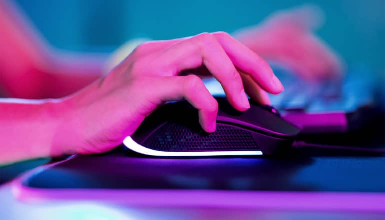 A person has their hand on a black computer mouse, their hand bathed in pink light, with blue light in the background