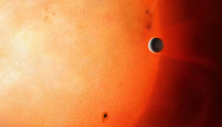 small planet appears just above the surface of a much larger, hotter star