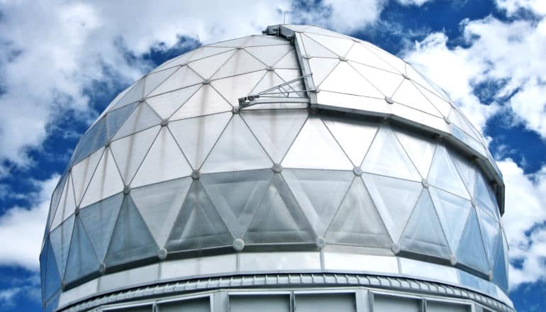 The metallic dome of the Hobby-Eberly Telescope stands against a blue, cloudy sky