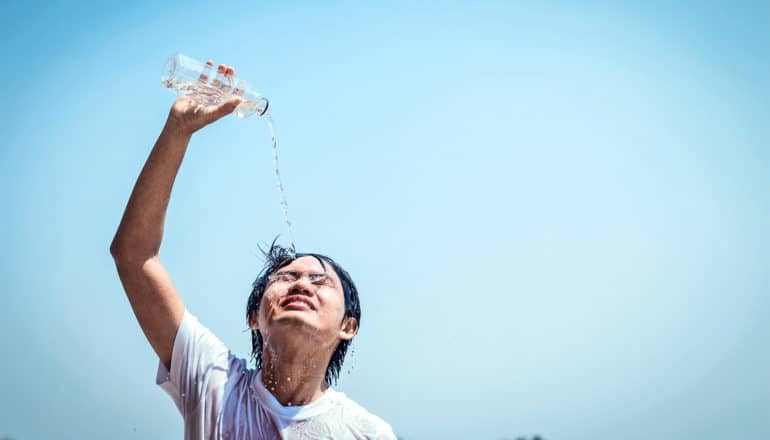 A young man pours water from a plastic bottle over his head with the blue sky in the background