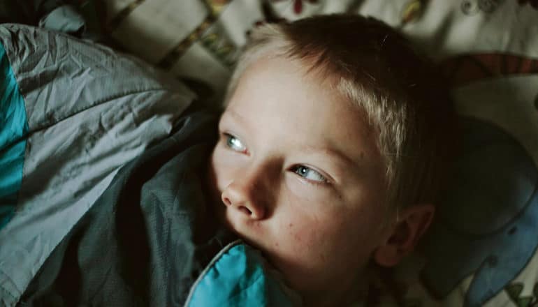 child in bed looks away, draws blanket up over mouth