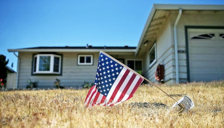 low-angle view of small US flag on dead lawn in front of house