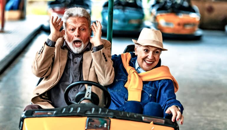 older couple in bumper car. He looks scared; she looks happy