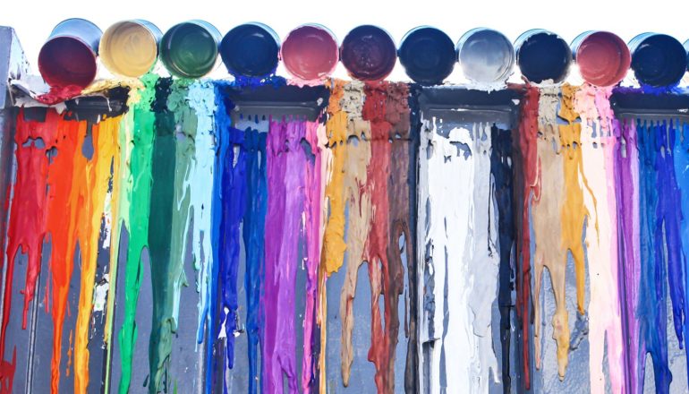 Paint cans on top of a wall spill their colorful contents down the wall