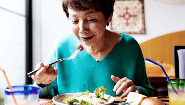 An older woman in a teal sweater eats a salad