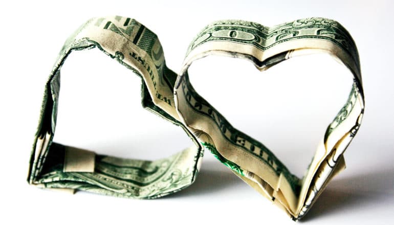 Two hearts made of 1 dollar bills lean against each other against a white background