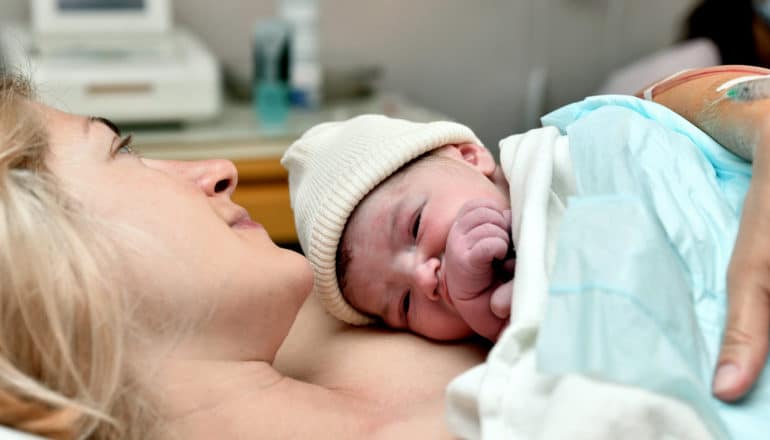 newborn in hat on mother's chest under blanket