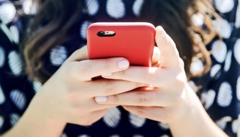 A woman holds a smartphone in a red case as she types with both thumbs